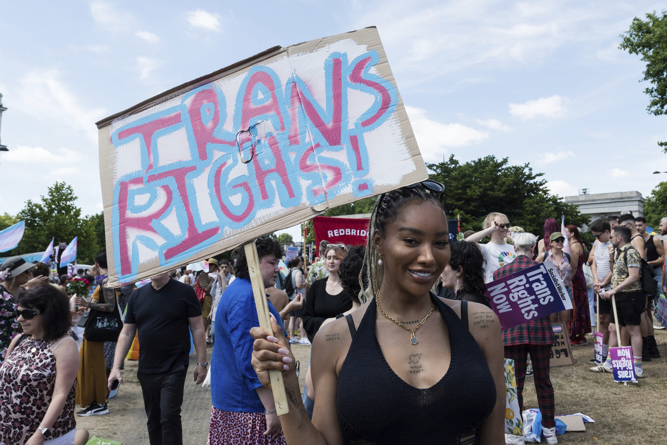 A Black woman smiles as she holds up a colorful "Trans Rights" sign at a Pride event in London.