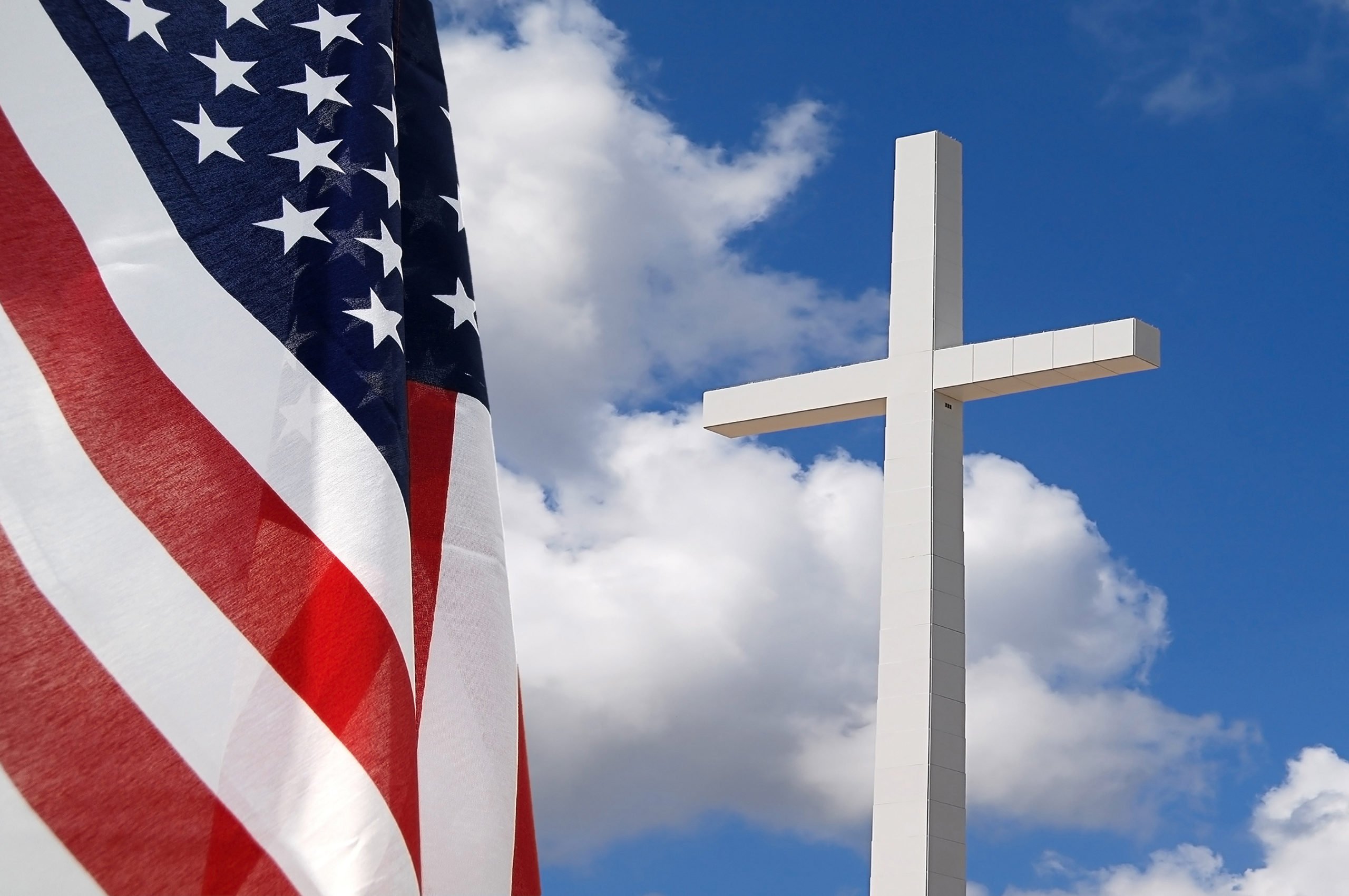 An American flag hangs in the foreground, upstaging a white cross.