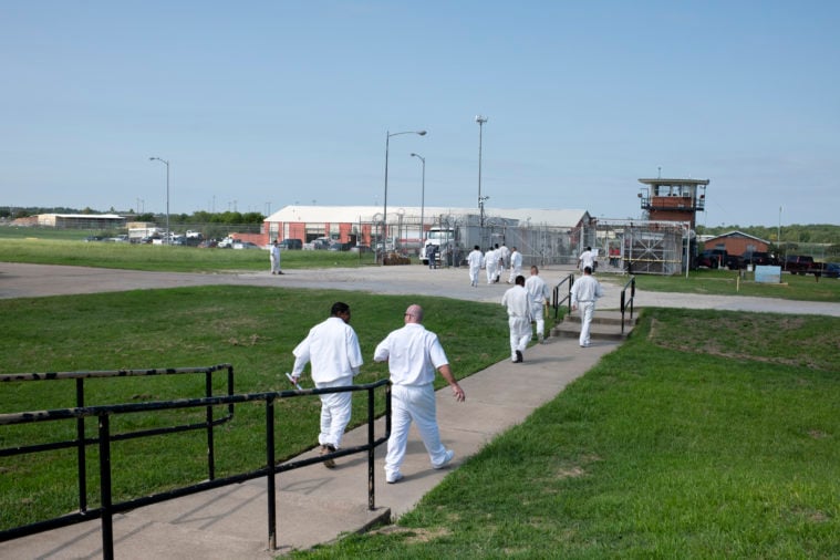 Prisoners in white prison uniforms walk across a grassy yard at Huntsville prison, where education programs now receive more funding.