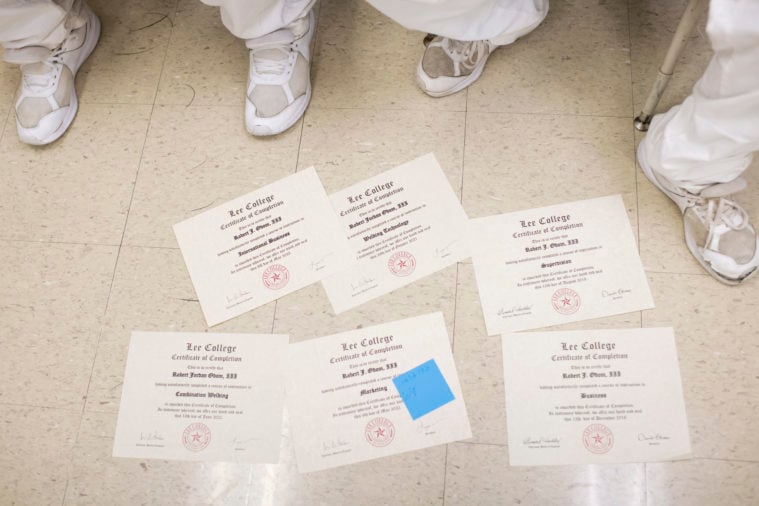 We see a scattering of Lee College certificates on the floor, along with the sock-clad, sandaled feet of a couple prisoners.