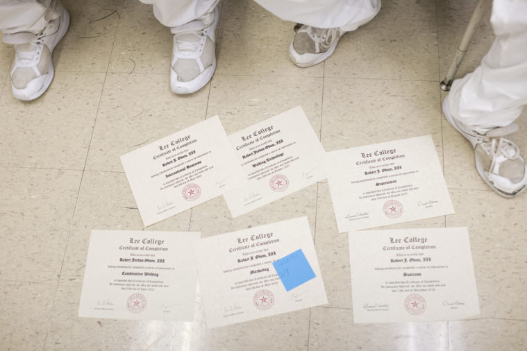 We see a scattering of Lee College certificates on the floor, along with the sock-clad, sandaled feet of a couple prisoners.