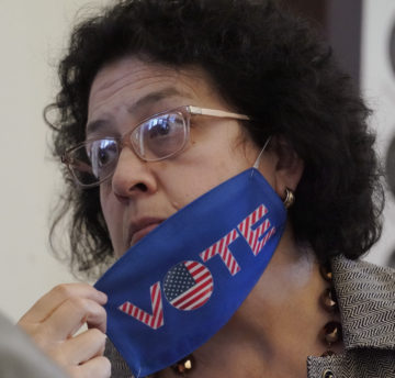 Celia Israel removes a red, white and blue VOTE facemask, wearing a serious expression.