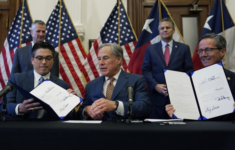 State Representative Chris Paddie fumbles with a reproduction of a bill to improve the reliability of the power grid, as Greg Abbott looks on.