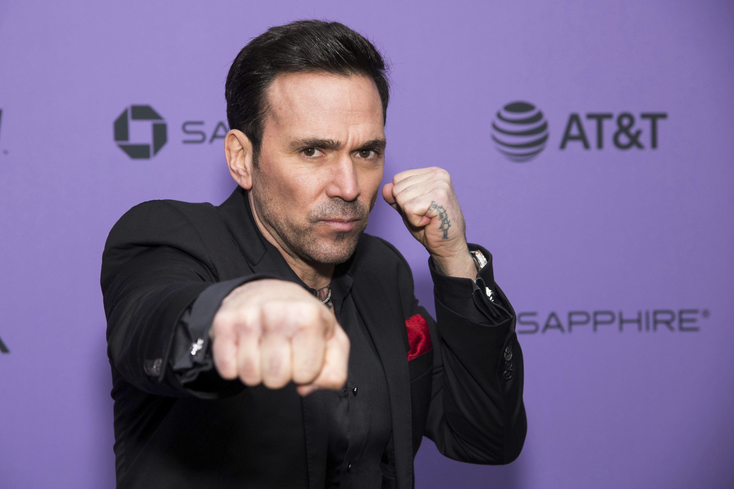 Dressed in black, Jason David Frank does a martial arts-style punch towards the camera, with his other fist held near his face in a defensive position.