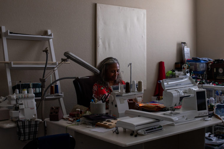 A comfortably cluttered workspace, with Jones at the center working on a sewing machine. Around her are fabrics, spools of thread and other supplies.