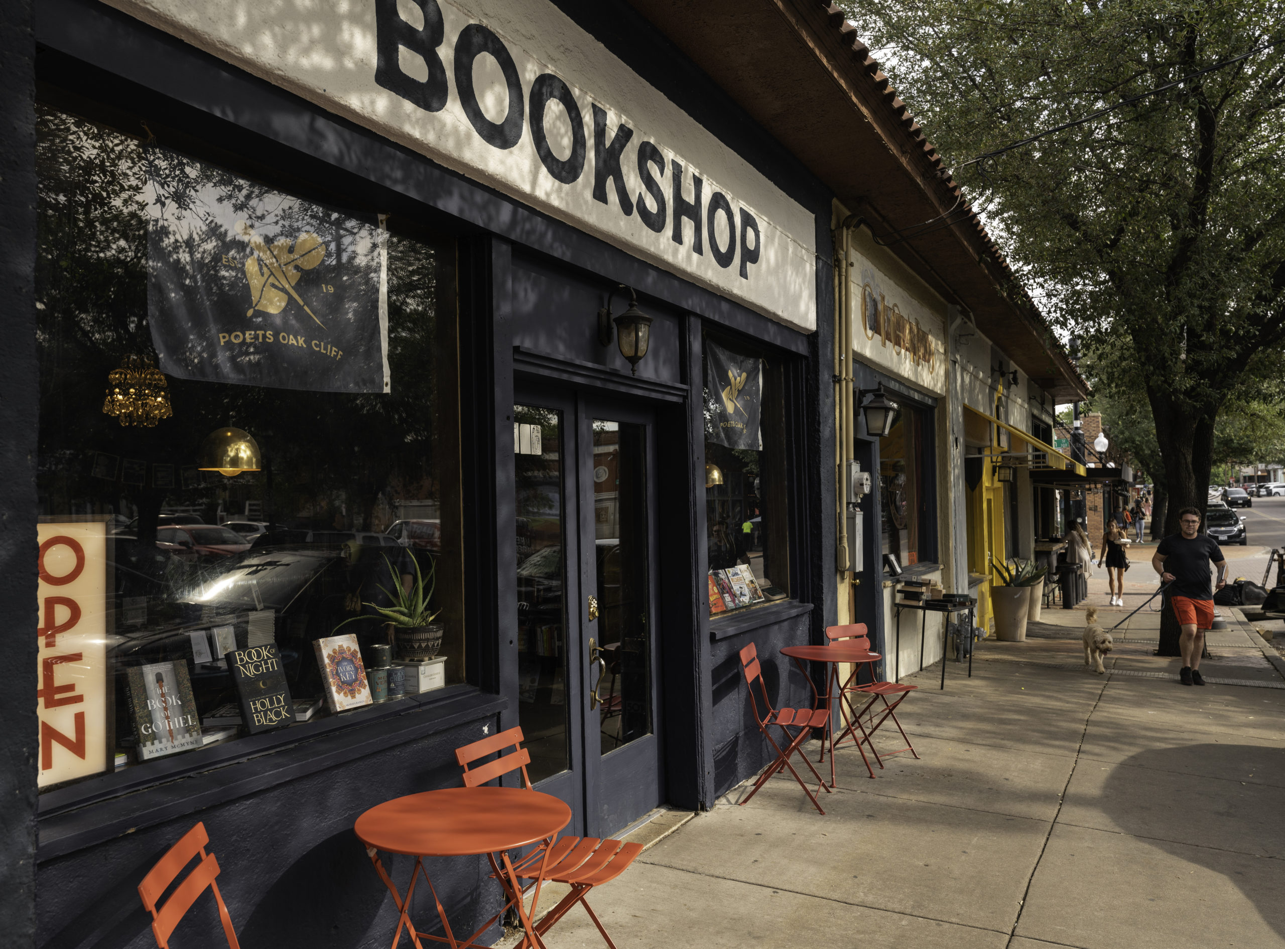 The facade of a shop in a row of shops, with a sign reading "bookshop" in clear block letters. Books and an Open sign are displayed in the window. Texas bookstores, and books about Texas, thrived in 2022.