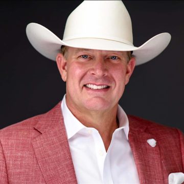 A portrait of Bobby Lindamood, a smiling white man in a white cowboy hat, light red suit jacket and white dress shirt.