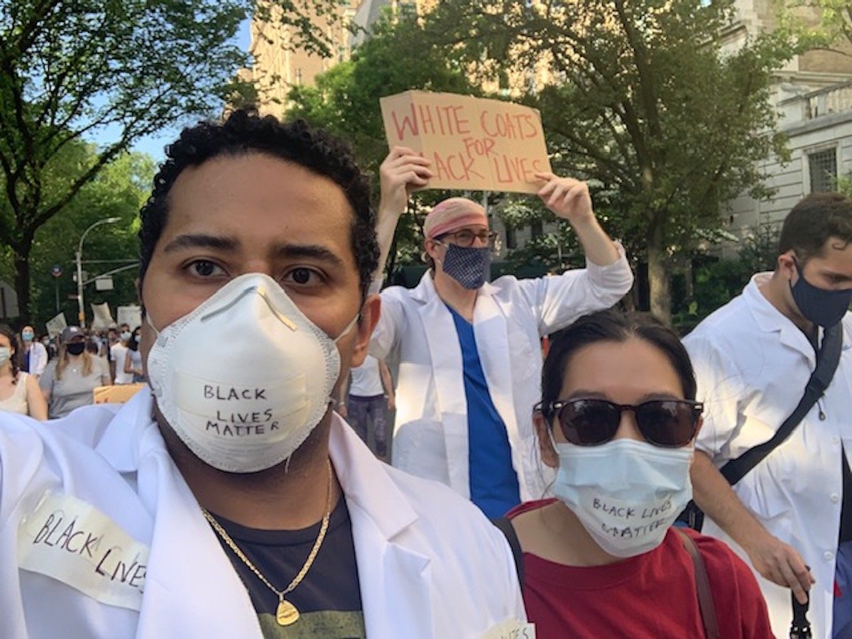 Christian Pean, brother of Alan Pean, marches with other medical professionals in a protest for Black lives affected by police violence. One sign held aloft by a protester reads "White Coats for Black Lives".