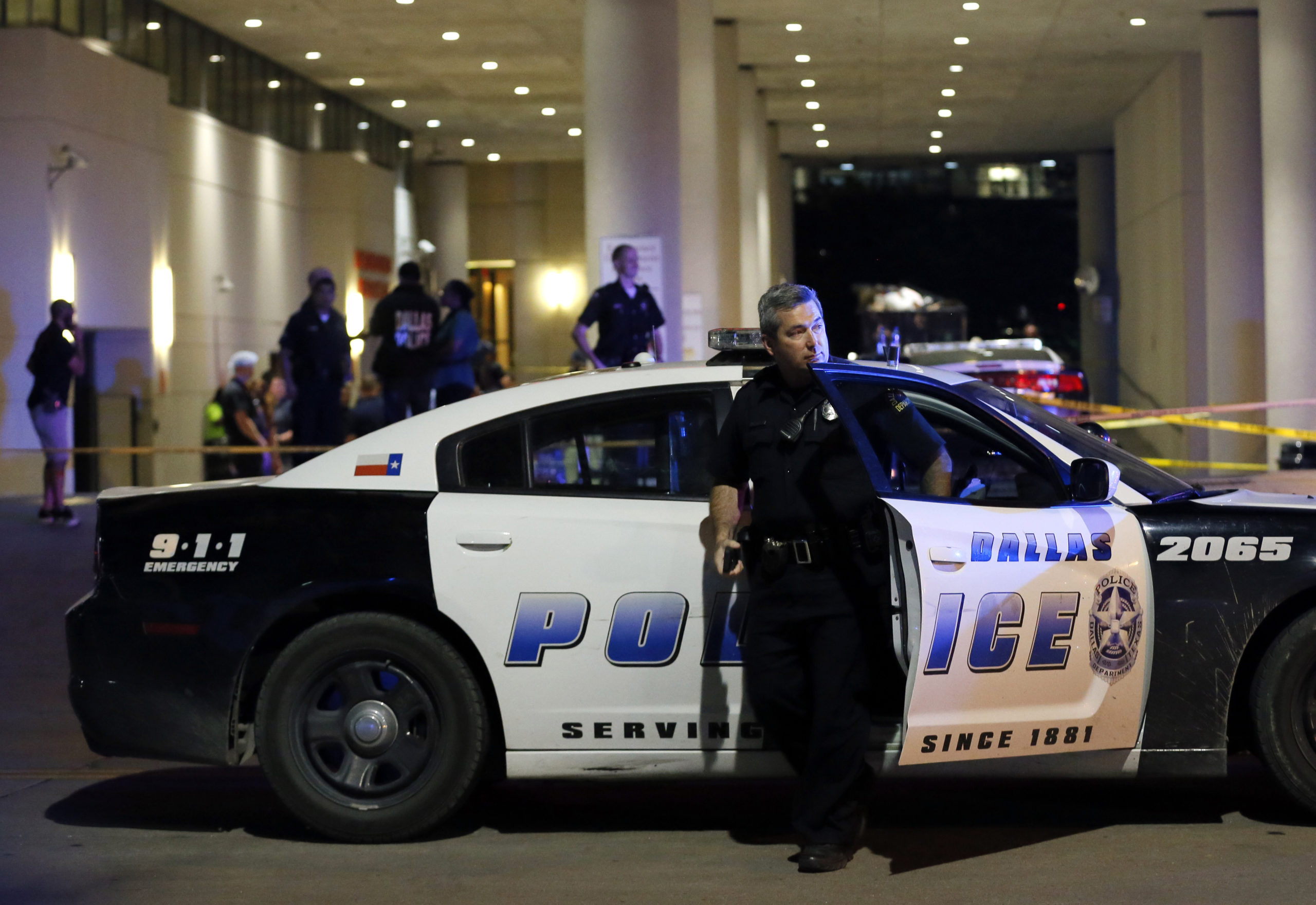 A white Dallas police officer steps out of the passenger side door of a cruiser, marked with Dallas Police department insignia. In Texas police budgets far exceed those for community services.