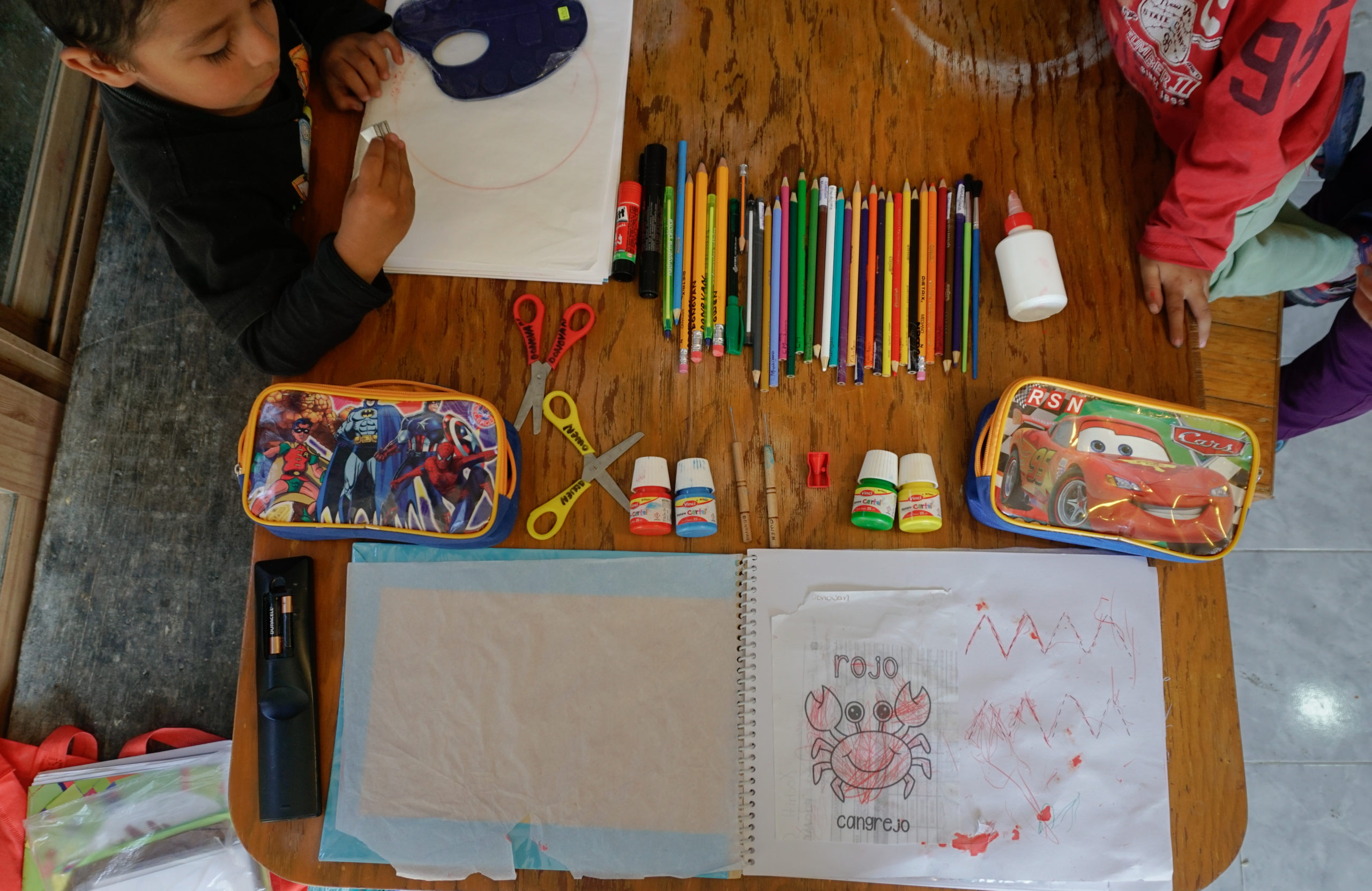 An array of school supplies including cartoon pencil cases, pencils and pencils and other sundries, surround a kid's drawing on a desk.