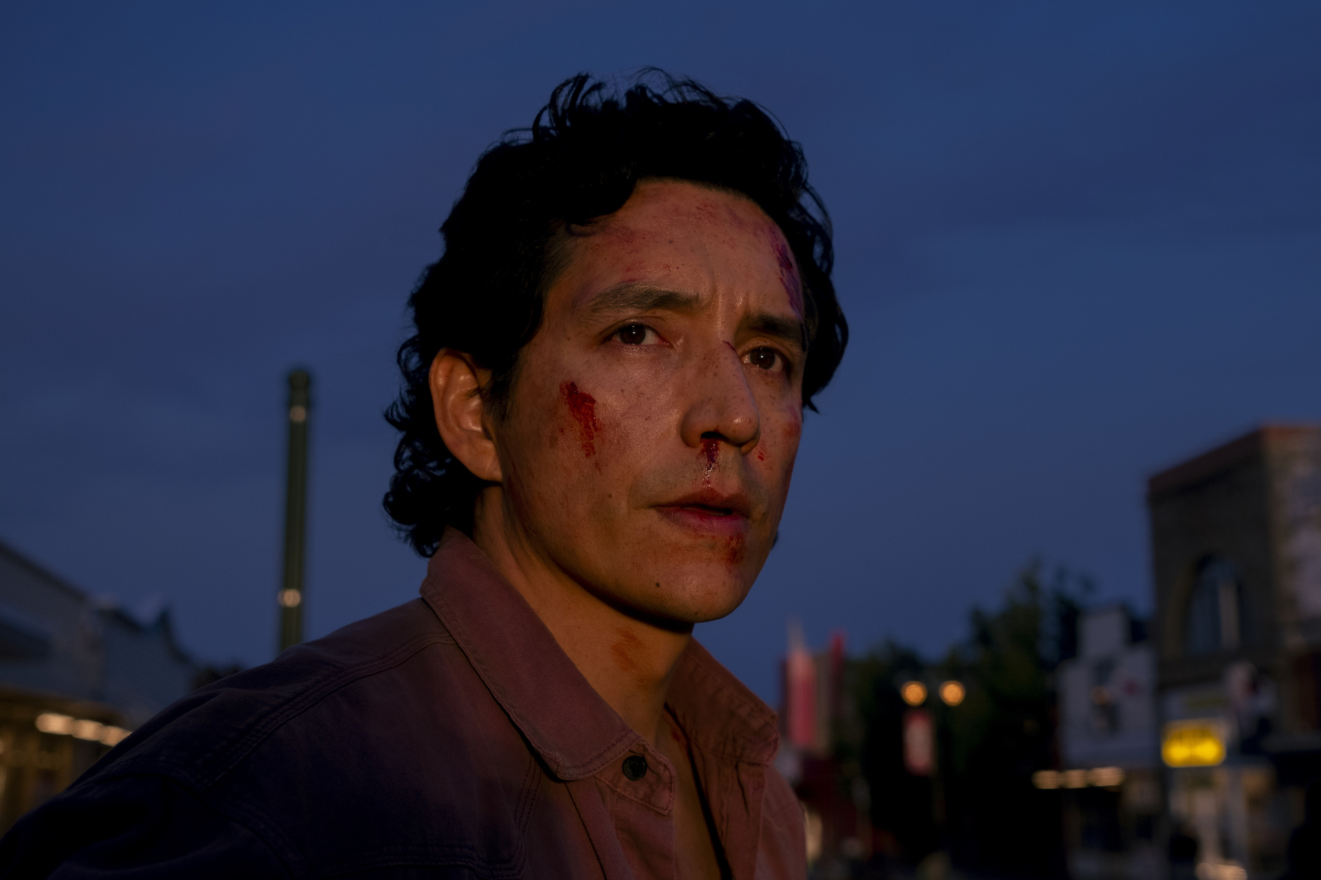 In a dark, dusky shot, Gabriel Luna stands in an urban environment with a serious expression on his bloodstained face.
