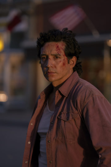 Gabriel Luna wears a serious expression on his bloodstained face. He's in an open casual button down with a white undershirt underneath.
