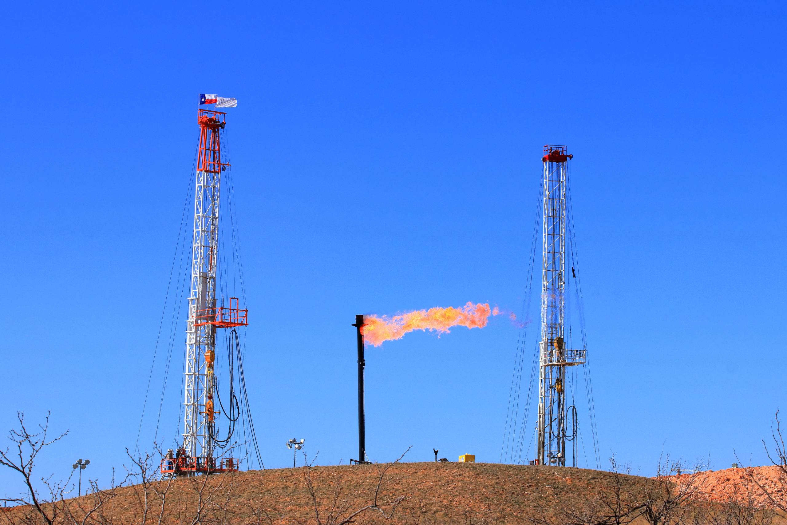 A flare goes off from a smokestack between two drilling rigs on a small hill in a West Texas oil field.