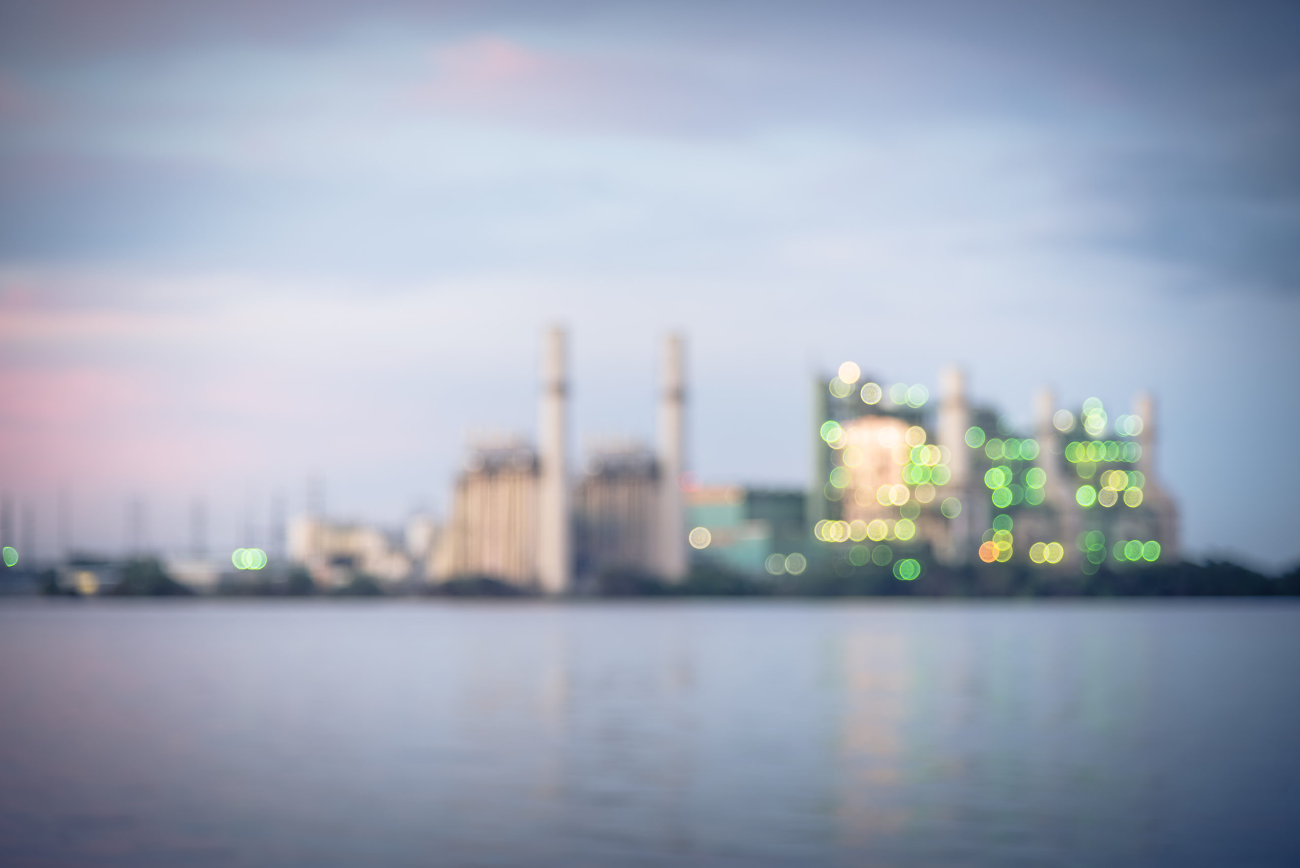 A deliberately blurry photo of a coal power plant in San Antonio, Texas, with a cooling pond in front of it. The coal plant is shot at dusk with a moody vignette filter.