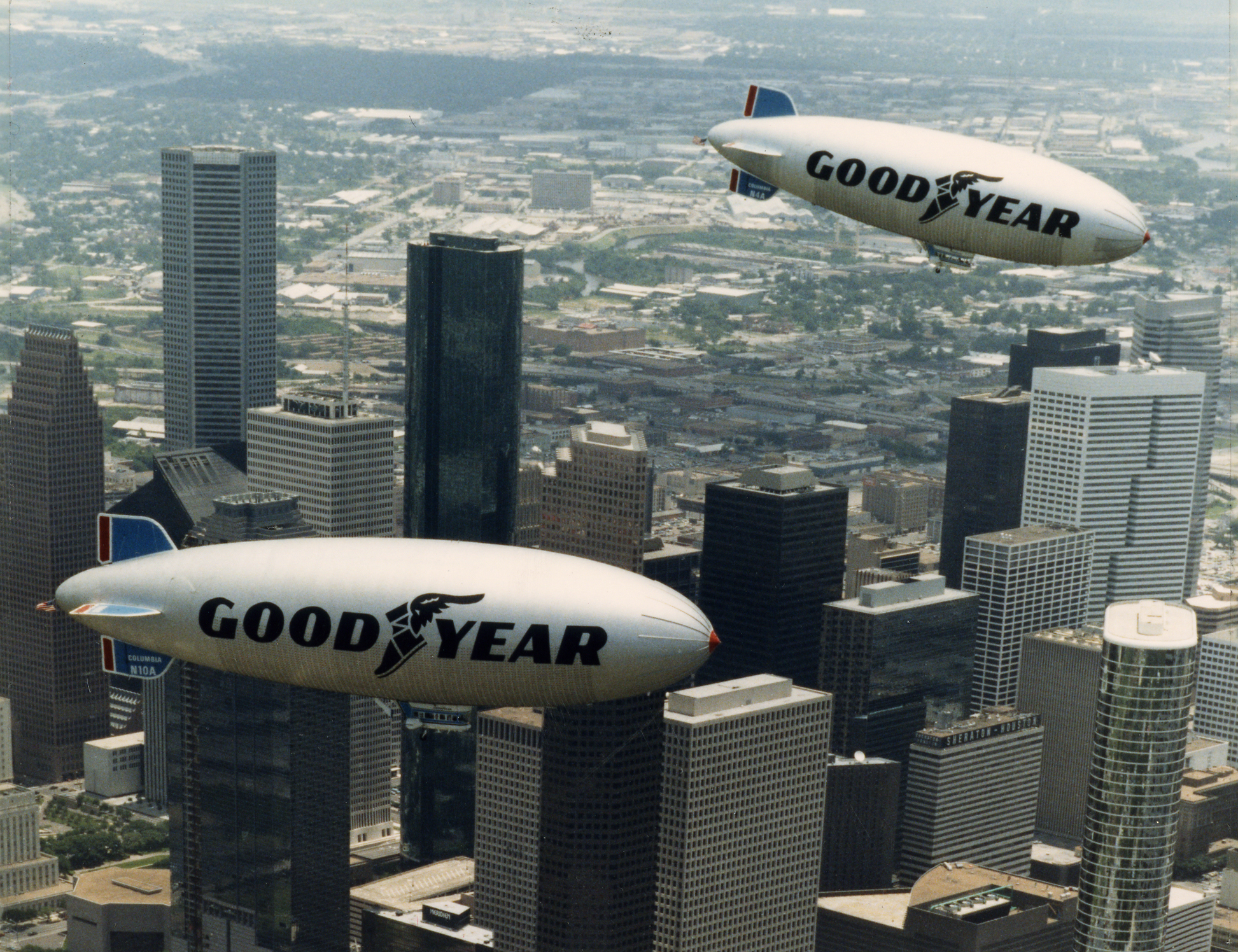 A historic photo of Houston's downtown in 1986, with two Goodyear Blimps floating over the tall skyscrapers.