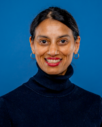 Rekha Lakshmanan is wearing a black turtleneck and has black hair tied back in a pony tail.