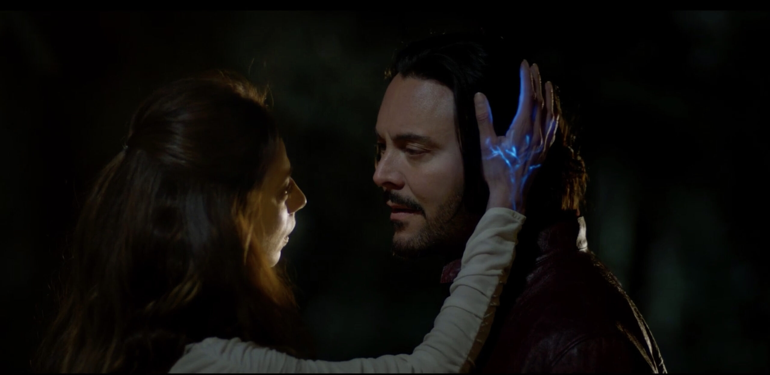 The Angel Gabrielle and Baal in Hail Mary. A woman touches a man on the face tenderly, and her hand is glowing with a strange blue light.