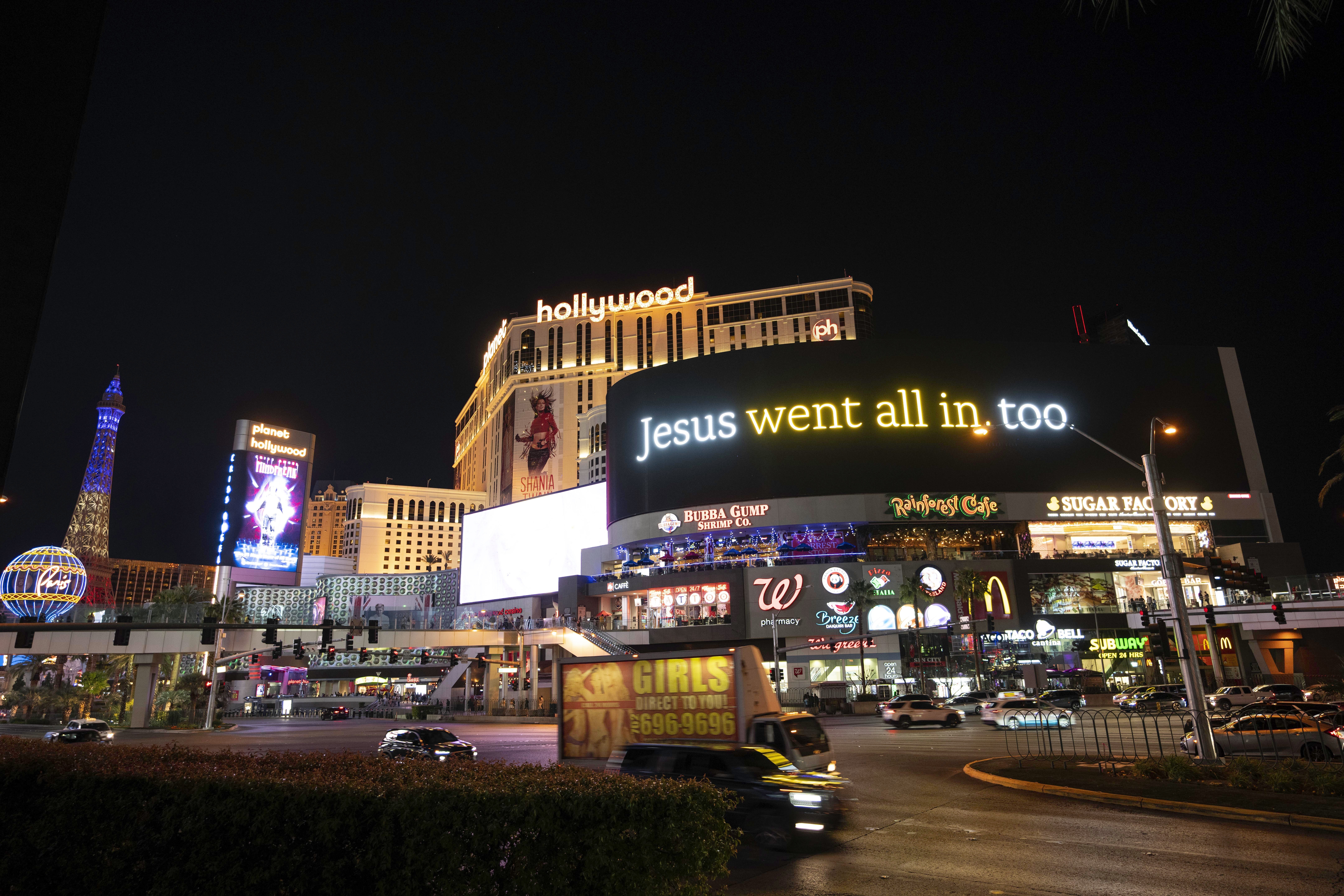 A lit billboard for the He Gets Us campaign seen in Las Vegas on the strip at night. It reads "Jesus went all in, too."