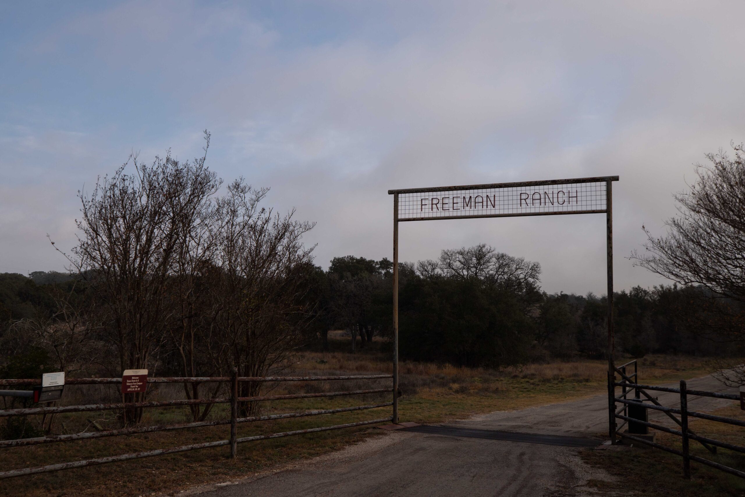 The sun is low over the Freeman Ranch gate, with a dirt path leading into the body ranch.