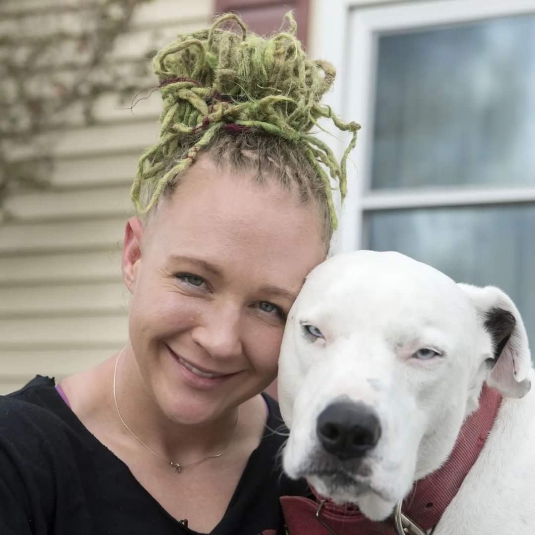 Reality Winner, a white woman with dreadlocks held up in a bun, poses smiling with a white bulldog.