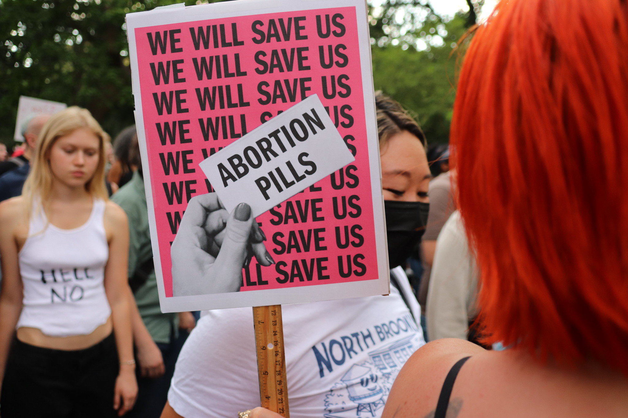 A sign from a reproductive rights protest with text "We will save us" along with a hand holding a card that says, "Abortion Pills."