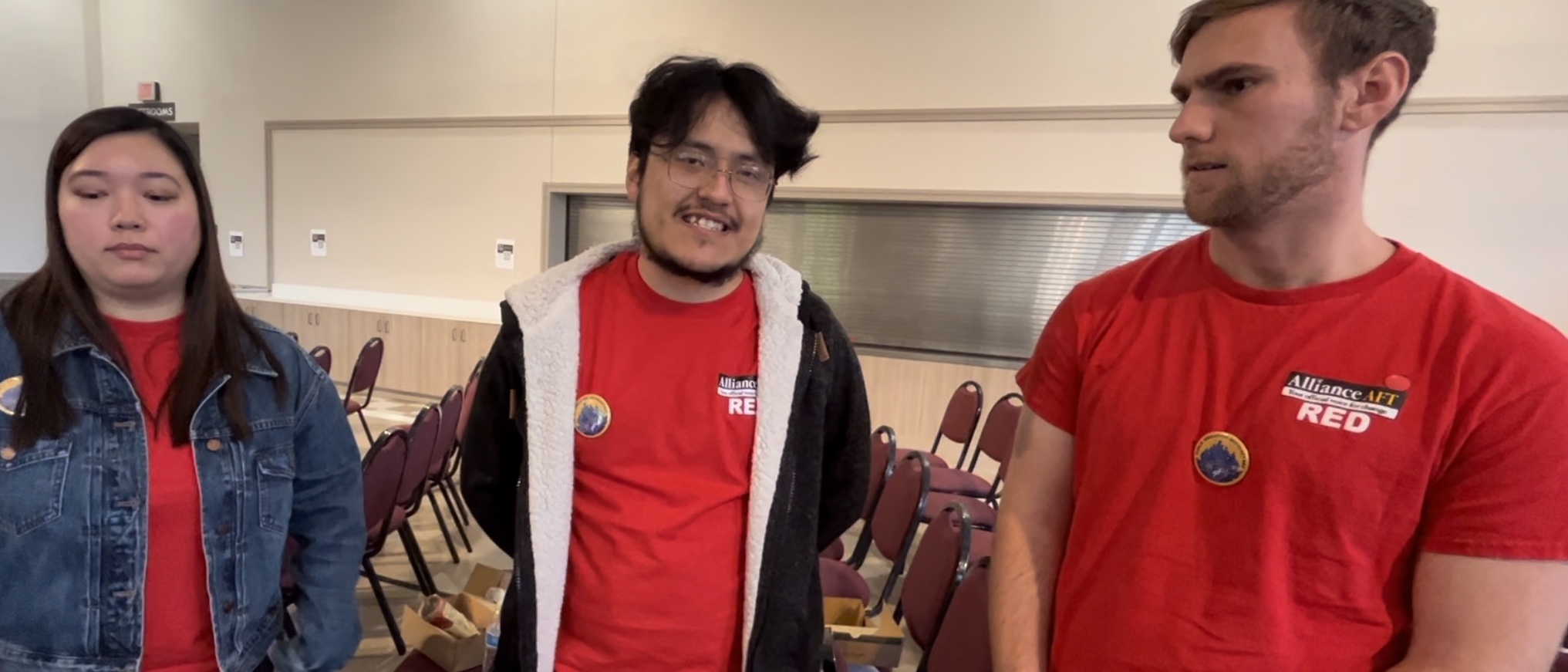 Three people in Alliance AFT Red t-shirts pose for the camera. The middle person is smiling while the one on the left side wears a denim jacket.