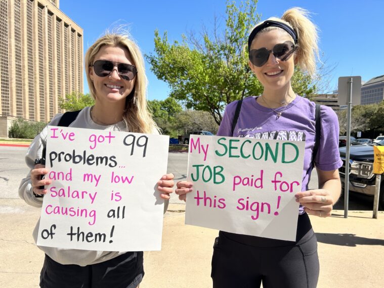 Two blonde women protest outside government buildings in Austin with signs reading: "I've got 99 problems ... and my low salary is causing all of them!" and "My second job paid for this sign!"