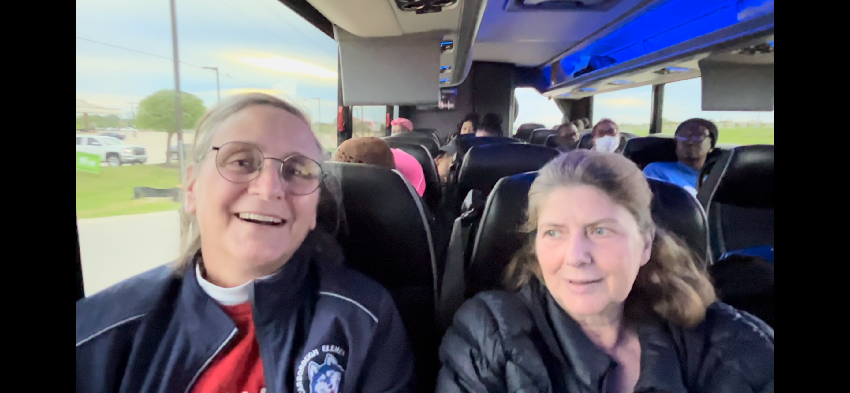 Two women sit together on a bus full of other teachers like them.