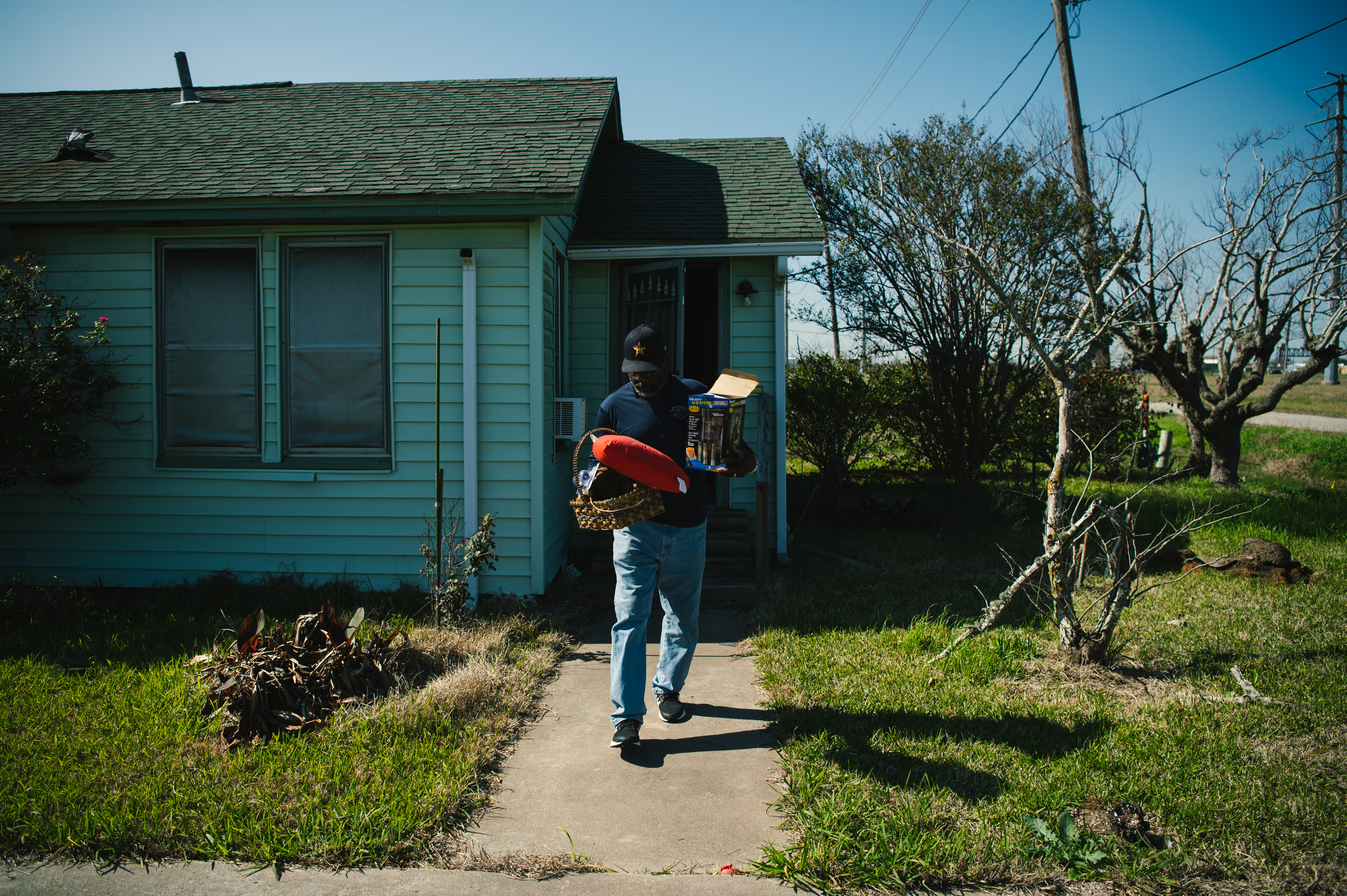 Kenny Jones, a Black man in blue jeans, dark blue shirt and matching cap, carries an armload of belongings out of the Henry Jones' home in Freeport, now condemned by the Port Freeport development.
