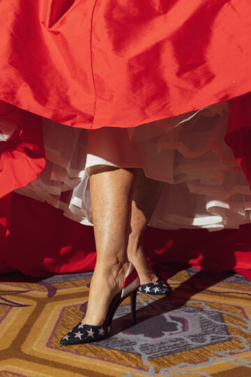 Seen from below the waist, a woman flares her red and white skirts to show off her US flag bedazzled pumps at the Ms Texas Senior America pageant.