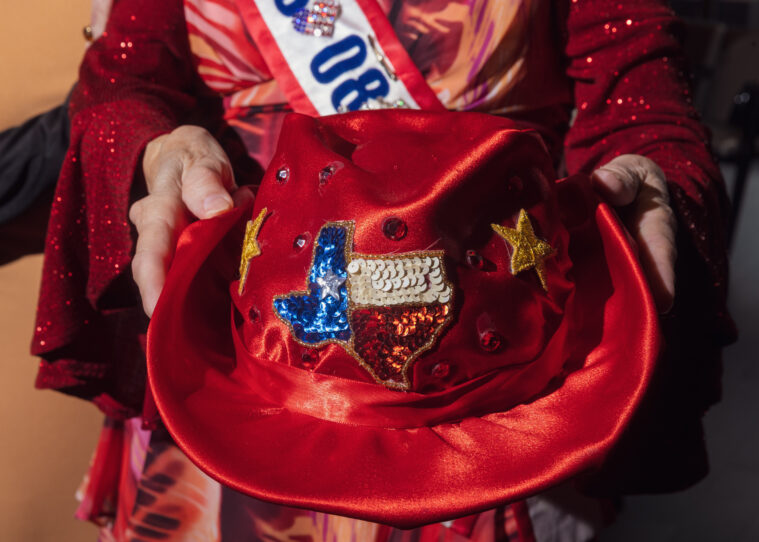 A woman holds a velvety red cowboy hat, bedazzled with red, white and blue sequins in the shape of the state of Texas.