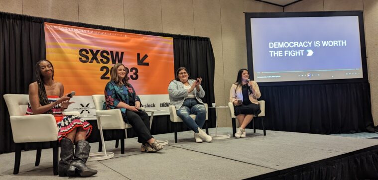 Four women sit on a panel at SXSW, prepared to speak into microphones. A slide reads, "Democracy is worth fighting for."