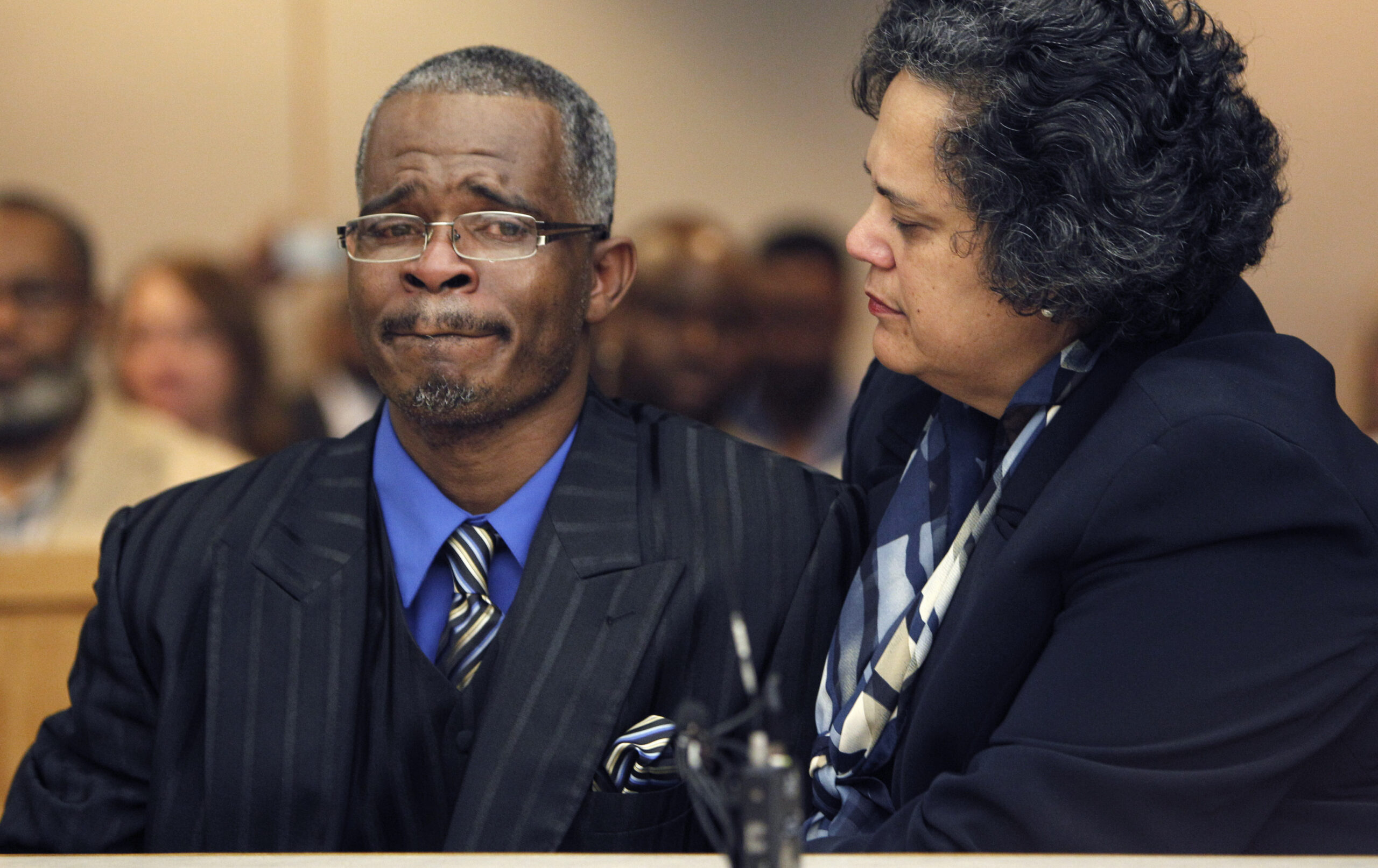 A Black man in a suit and tie is comforted by his lawyer, a Black woman also in formal dress, as the two stand in a courtroom. Richard Miles looks overcome with emotion.