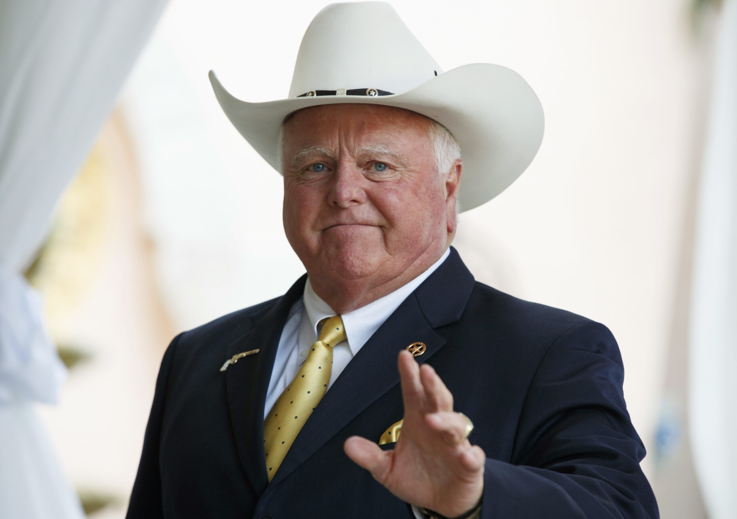 Agriculture Commissioner Sid Miller, a broad-shouldered white man in a white "10 gallon" cowboy hat atop his tailored suit and metallic gold polka dot tie.
