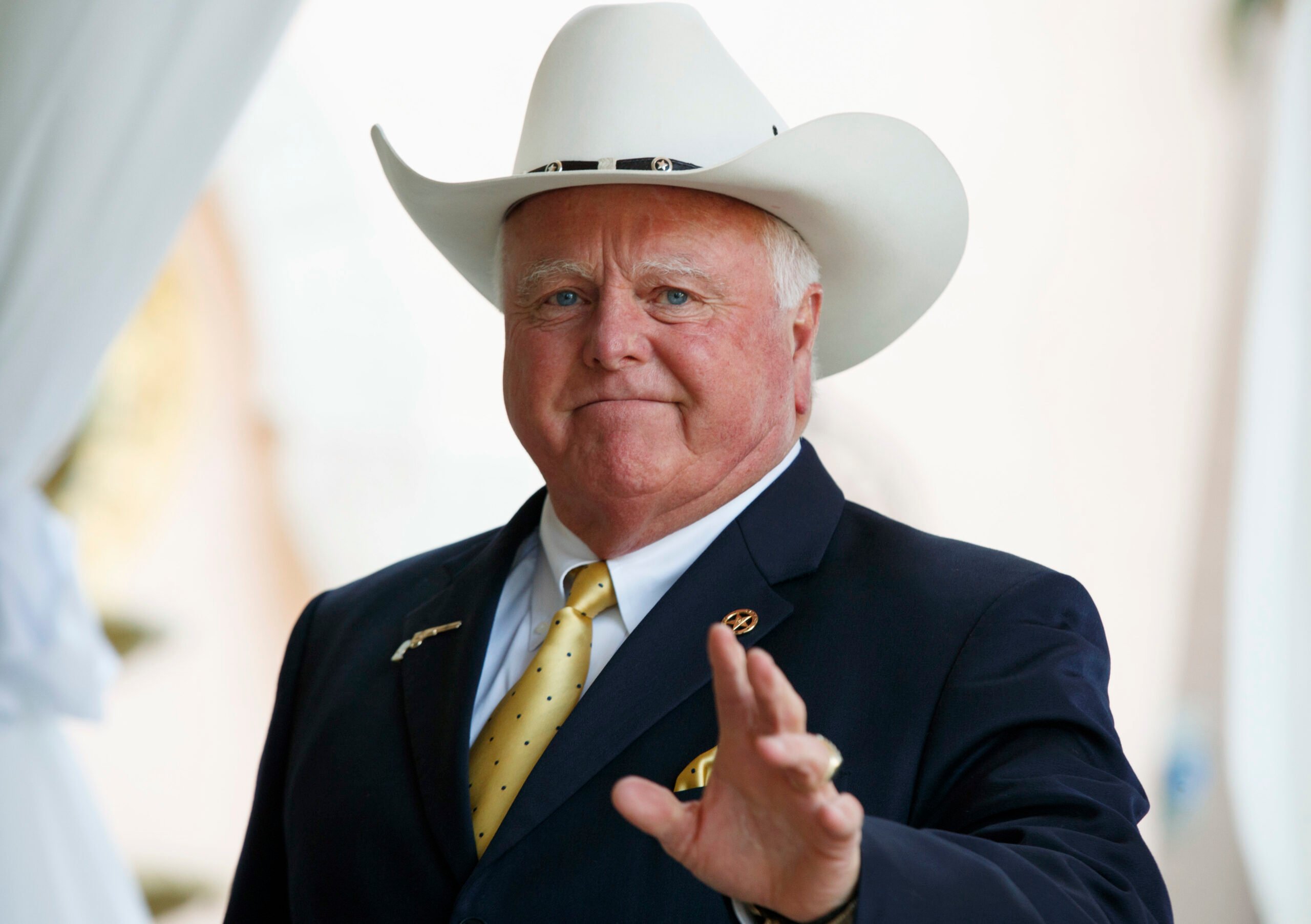 Agriculture Commissioner Sid Miller, a broad-shouldered white man in a white "10 gallon" cowboy hat atop his tailored suit and metallic gold polka dot tie.