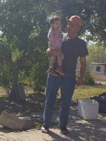 Antelmo Ramirez, a middle-aged Latino man, holds his young grandson outside.