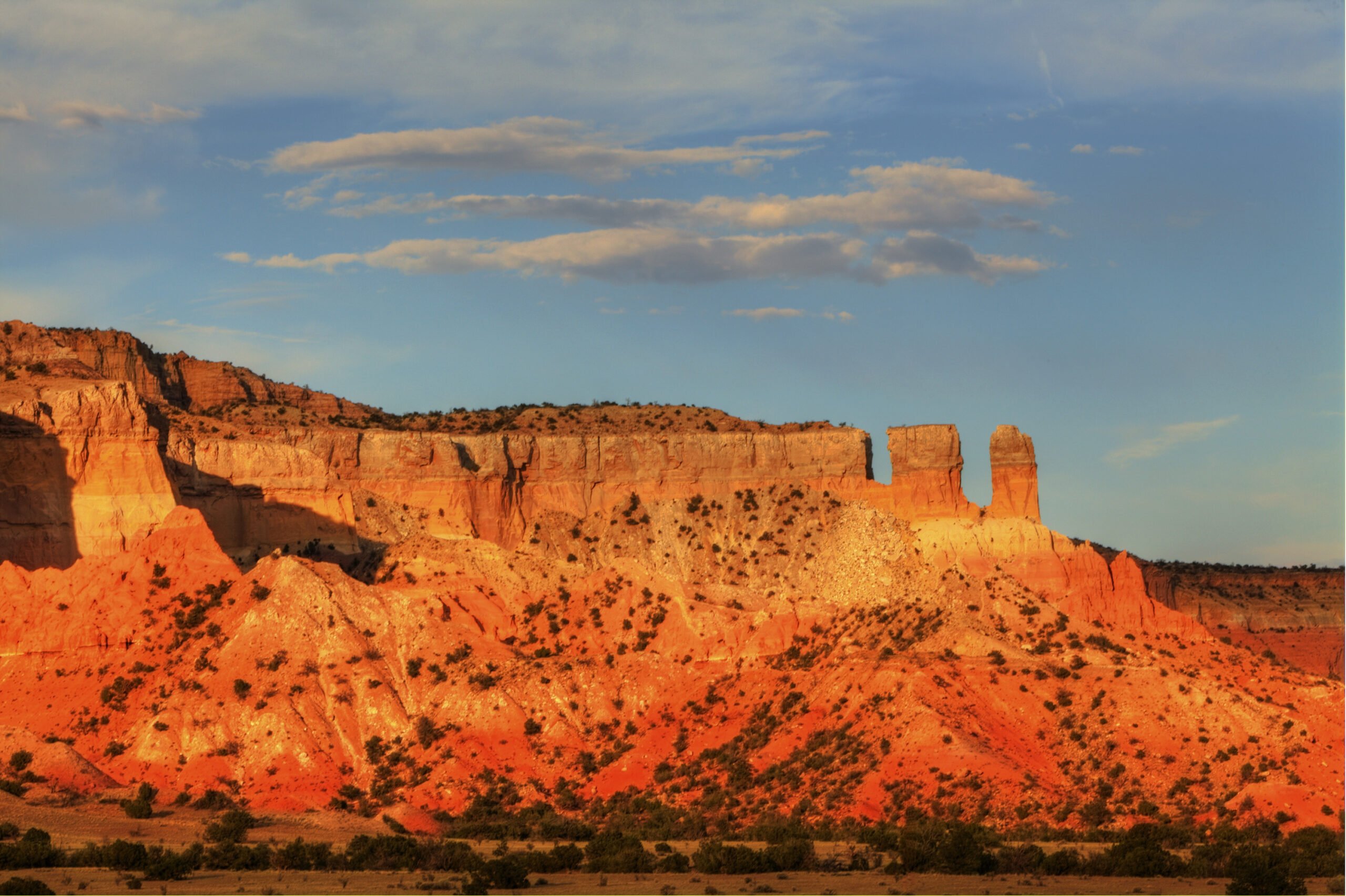 A sun-bleached desert landscape iin Georgia O'Keefe country, Abiquiu, New Mexico, with a huge mesa and scrubby bushes, reminiscent of Georgia O'Keefe's landscapes.