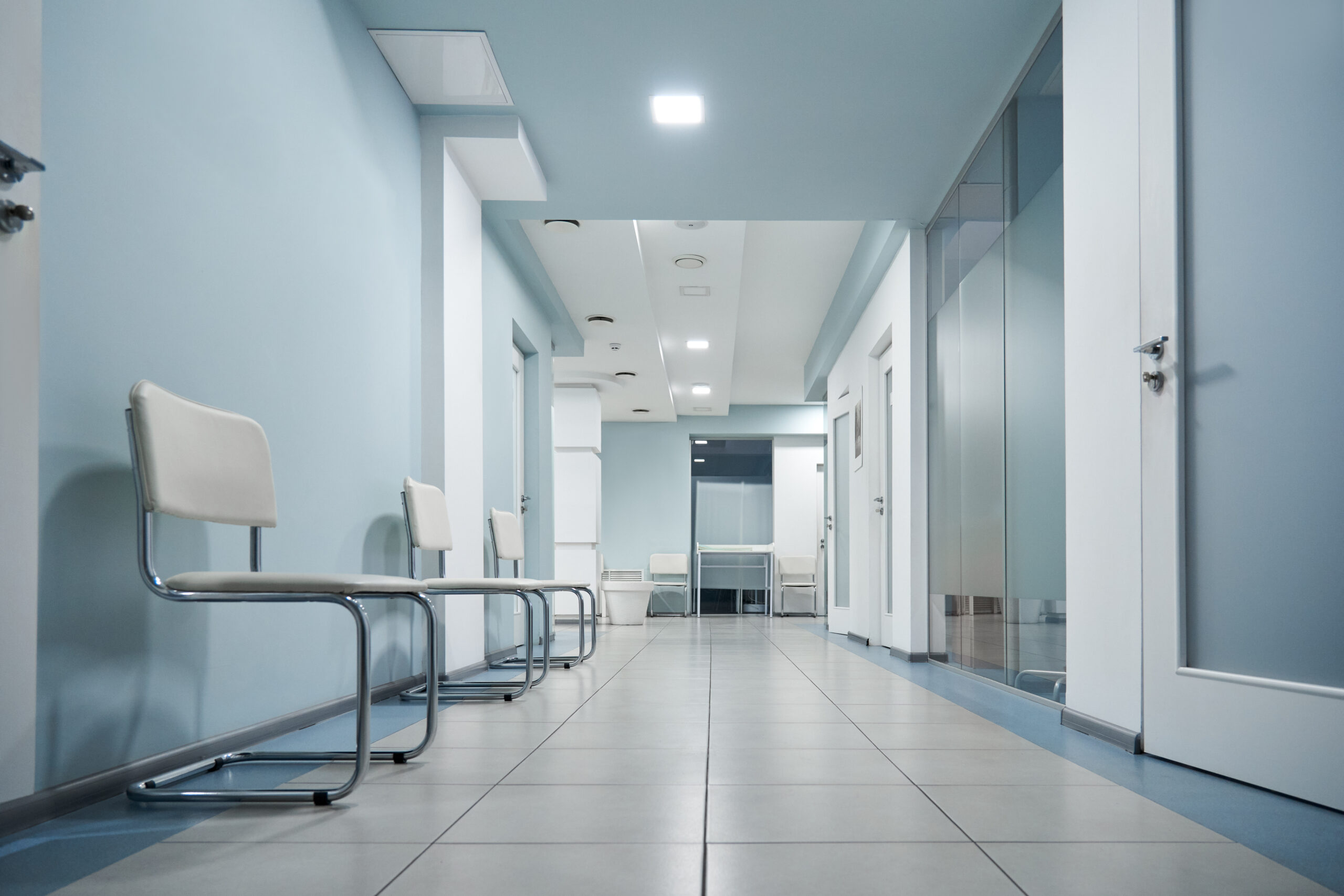 An empty hospital waiting room, with clean white walls and polished floors under bright white flourescent lights.
