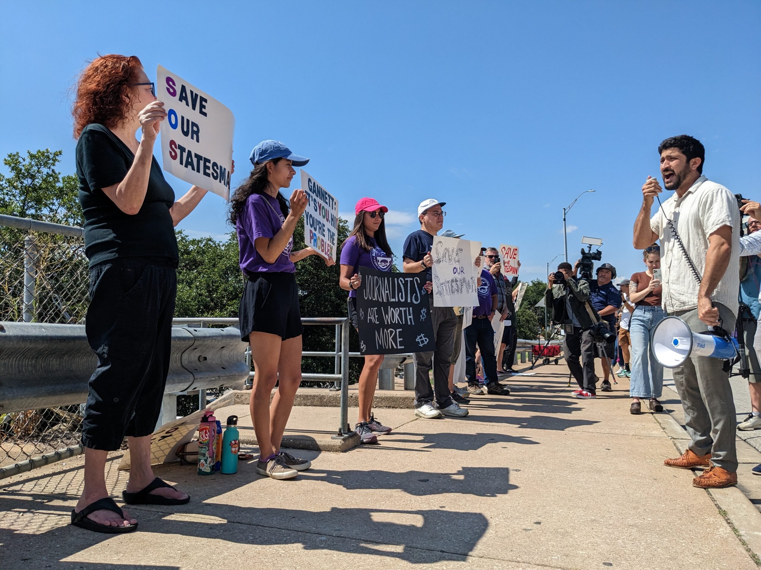 A row of Austin American-Statesman workers standing along the side of Congress Avenue bridge as Greg Casar, wearing a white shirt, addresses them.