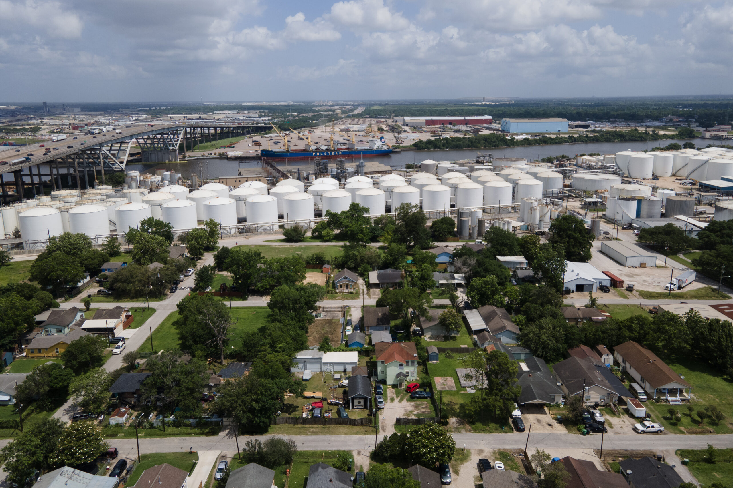 A drone image showing the Valero refinery, a series of white indutstrial tanks in clusters up against a residential neighborhood and a waterway which passes through Houston.
