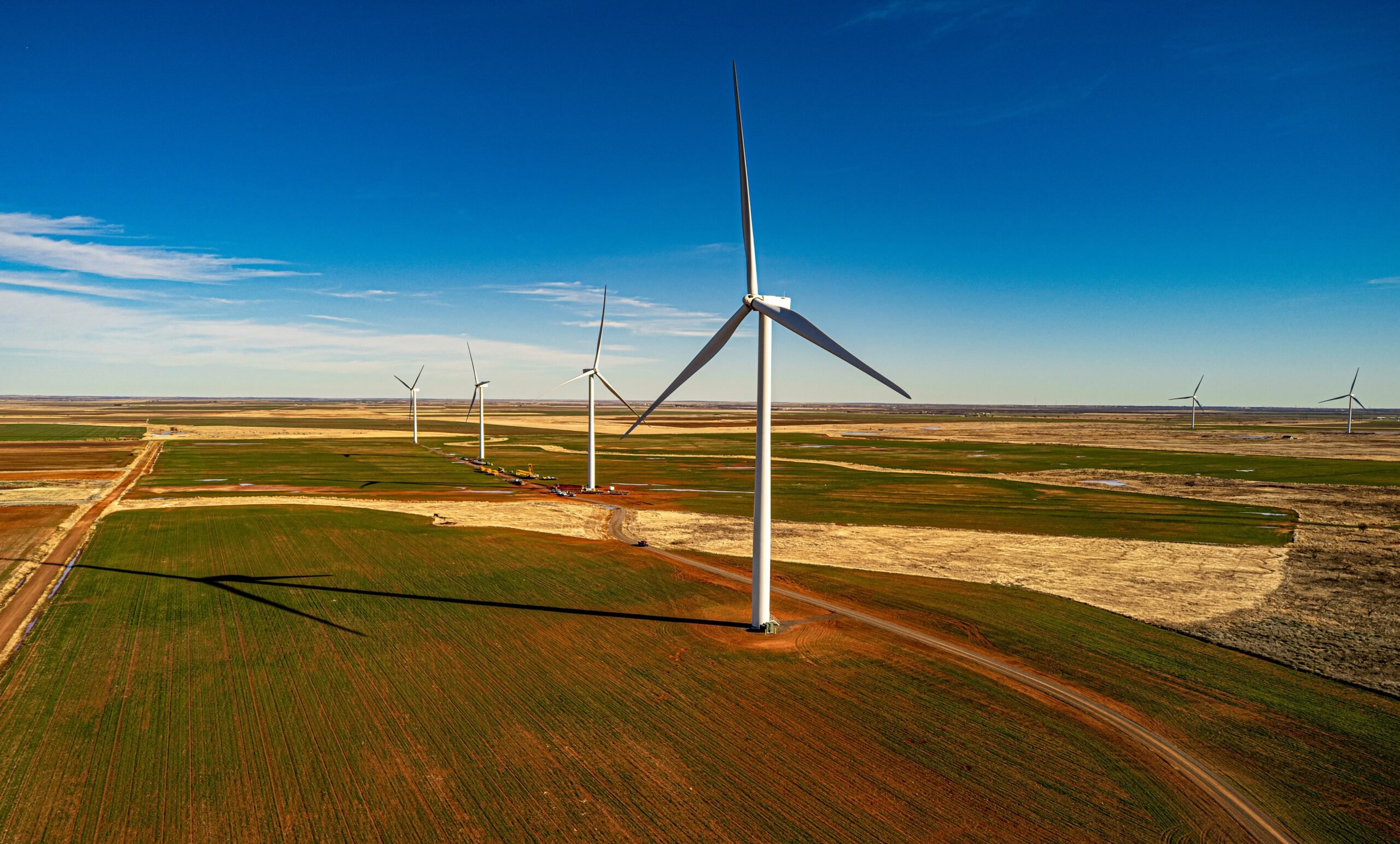 A wind turbine above fields in the flat North Texas landscape. The Taproot and the Climate and Community Project’s report for Texs recommends increasing offshore wind farming, canceling all existing utility debt, and creating community utility boards that establish public control over energy generation.