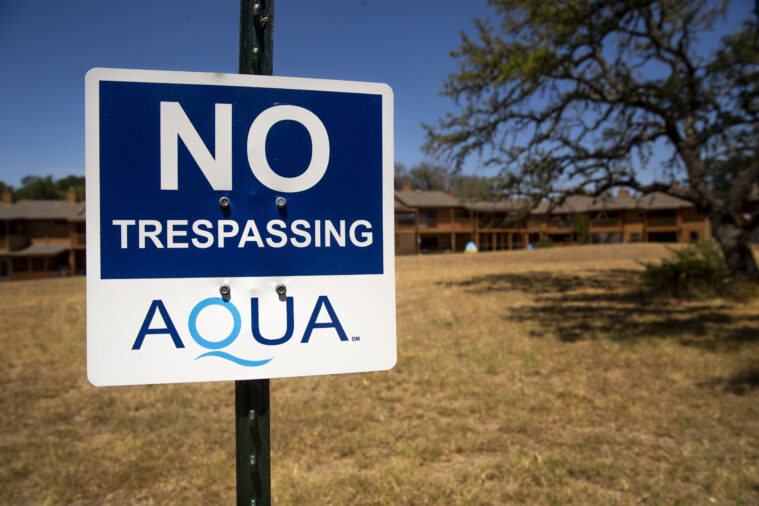 A sign in front of a dry field reads "No Trespassing" with an Aqua logo.