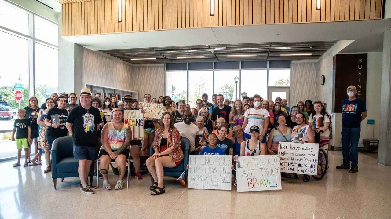 Dozens of people gather for a portrait, some holding signs in support of the queer community, such as "LGBTQ+ Kids are Truly Brave". 