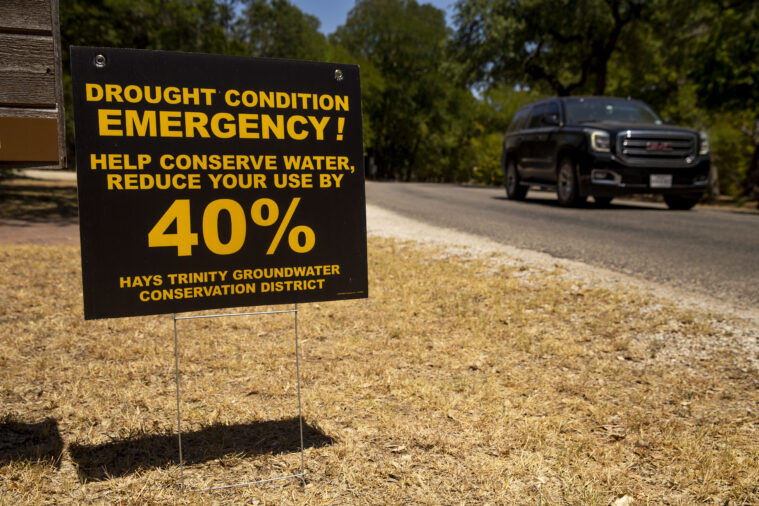 A SUV drives by a yellowing lawn with a sign warning water consumers to reduce usage by 40 percent during the drought emergency.