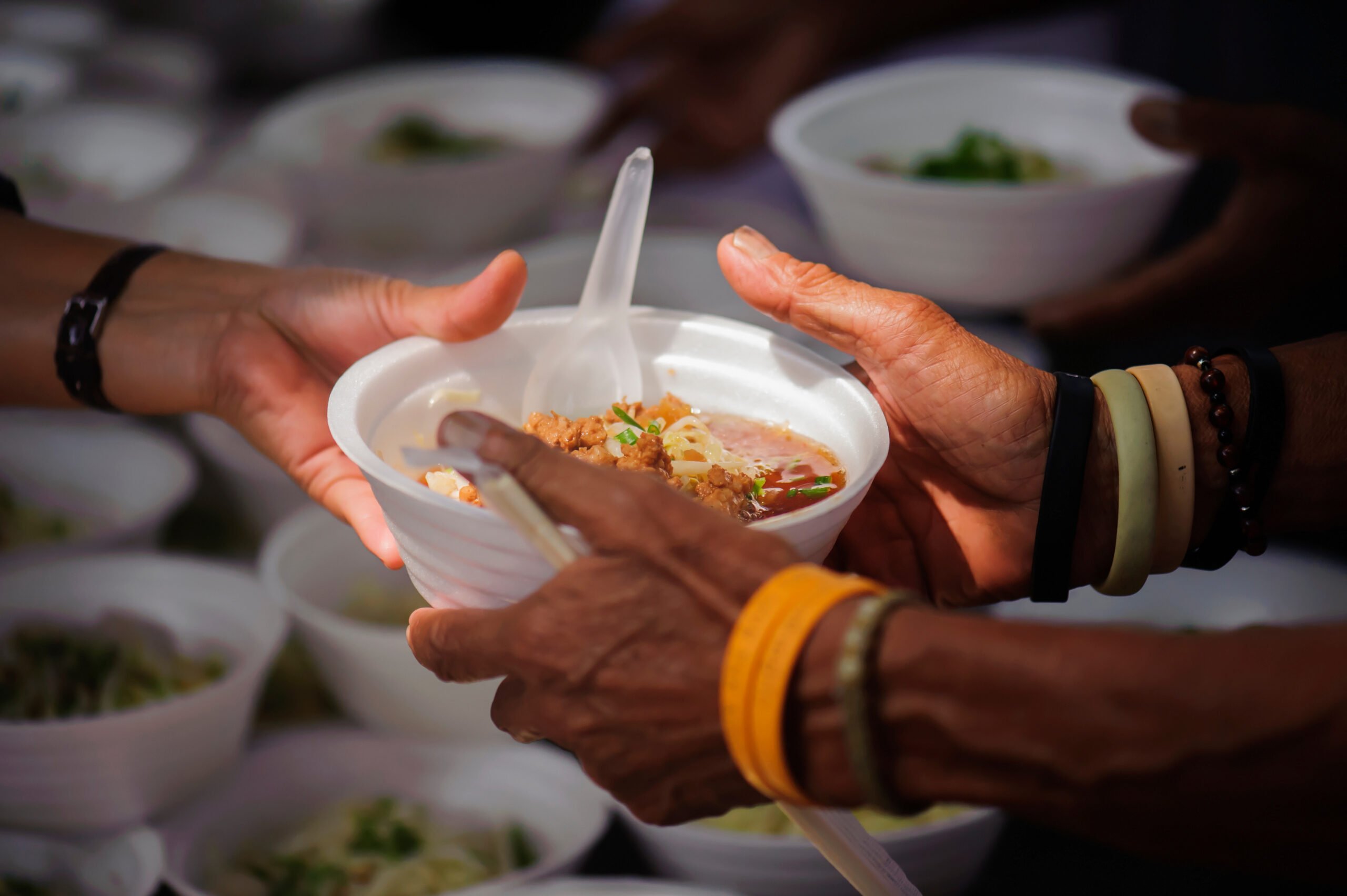 People sharing food. In this stock photo, similar to a Houston Food Not Bombs event, a volunteer hands a bowl of food to another person.