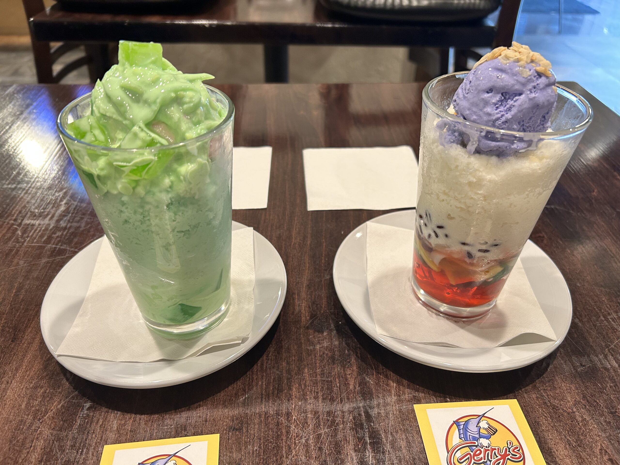 Two glasses of shaved ice on a table, with Gerry's Grill napkins displayed in front. The one on the left is lime green, while the other is red, white and purple at the top.