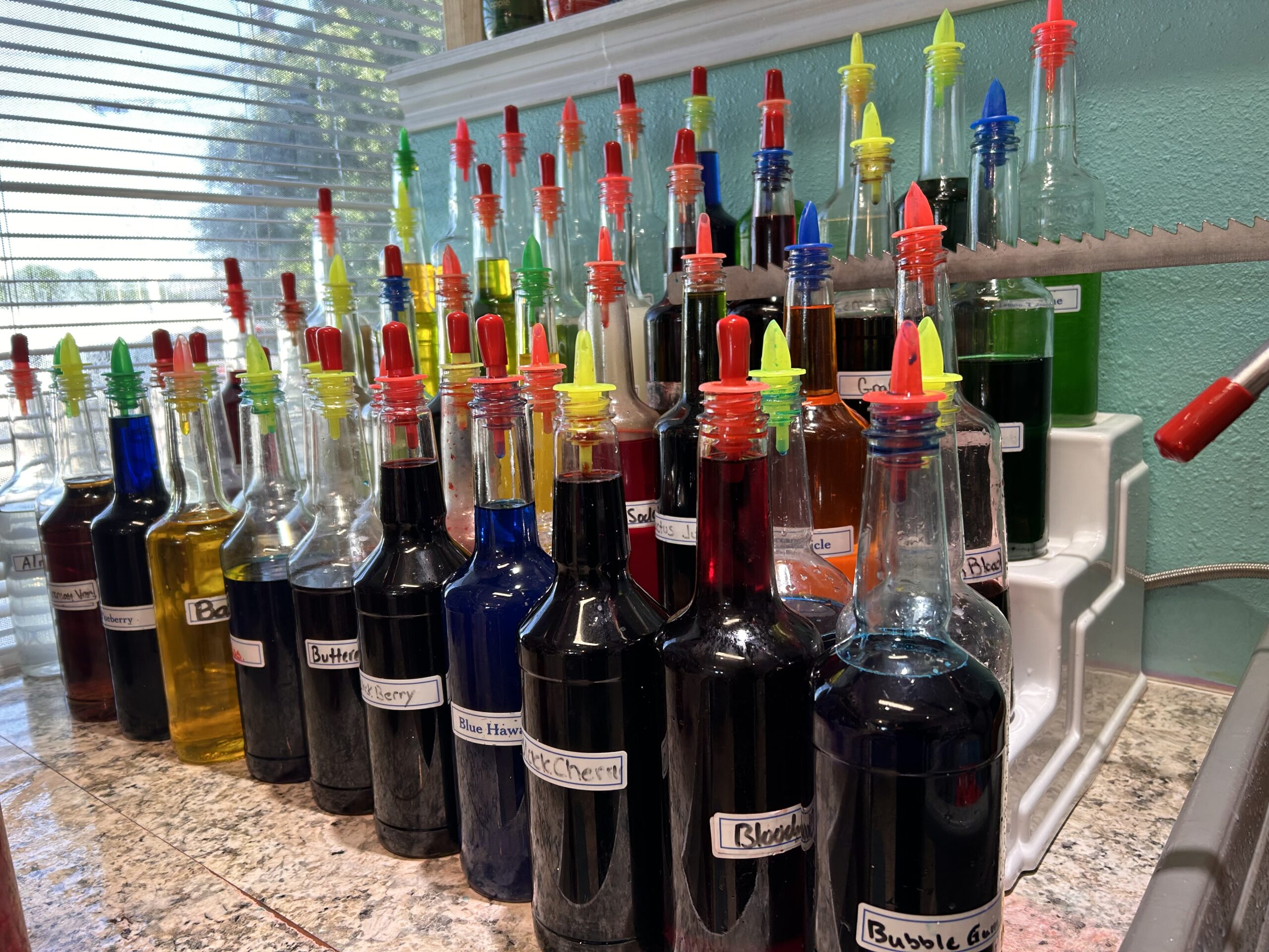 Dozens of labeled bottles containing colorful syrups, with easy pour tops, are arranged on the counter at Sno Dreamz.