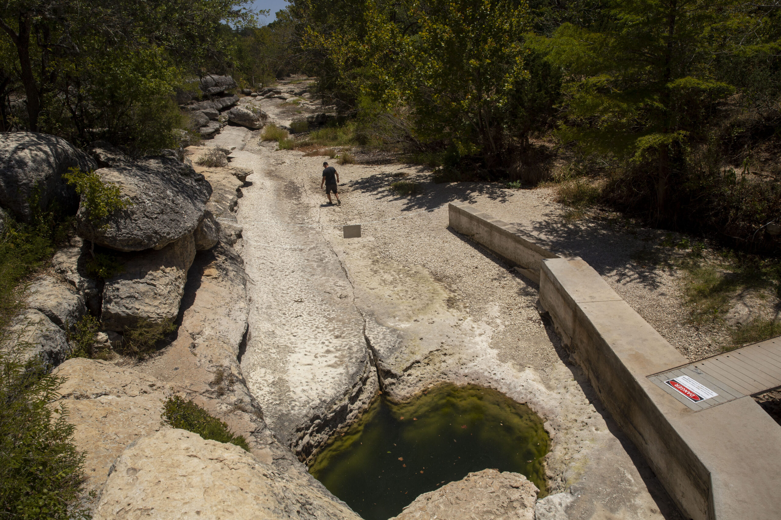 A lonely figure stands in a dry spring bed, usually full of gushing fresh water. There are drought-struck trees all around the "well" of Jacob's Well.