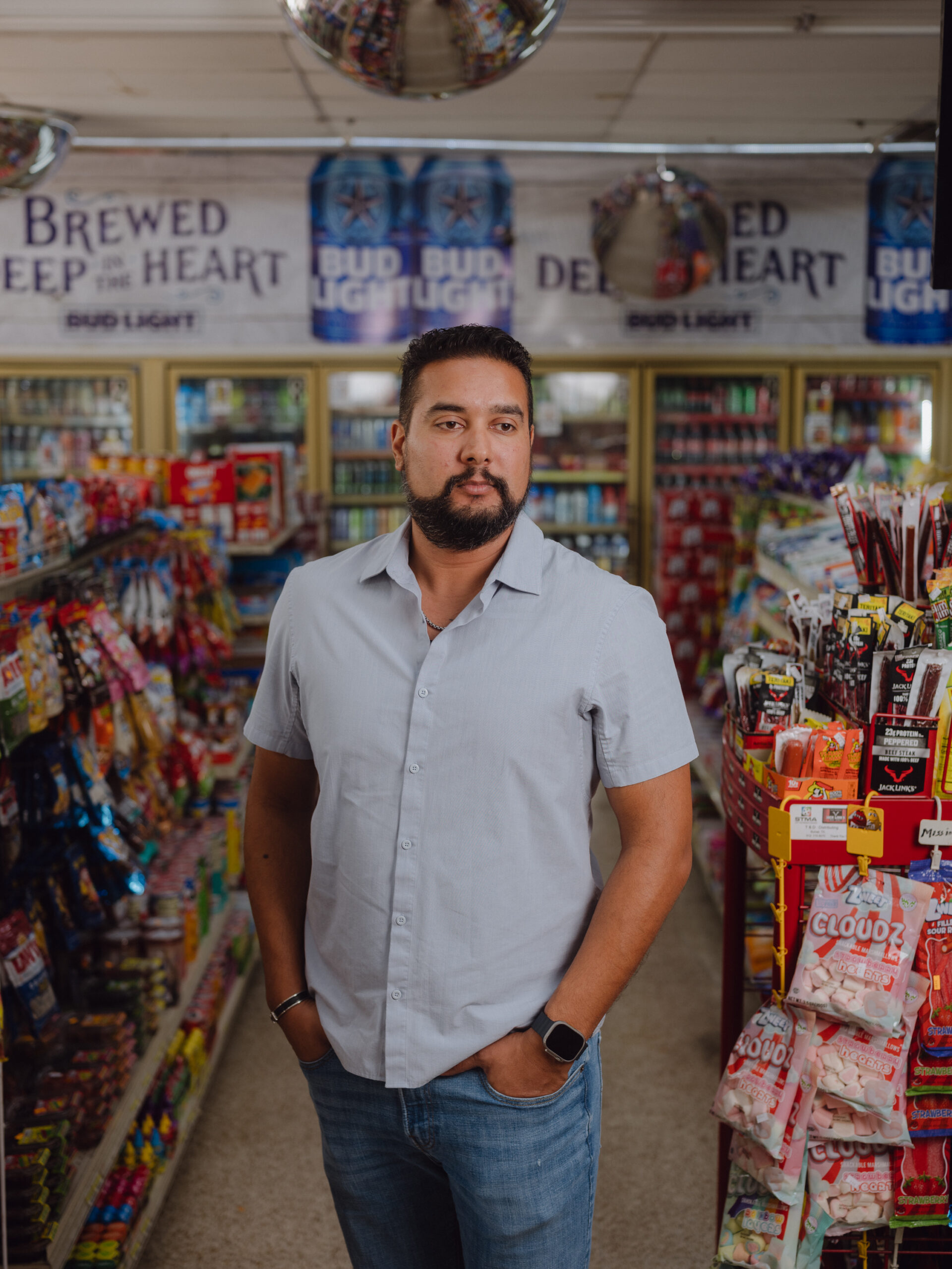 Mitesh Patel, in jeans and a blue button down, poses in an aisle of the convenience store where his father Hasmukh was murdered by Christopher Young.