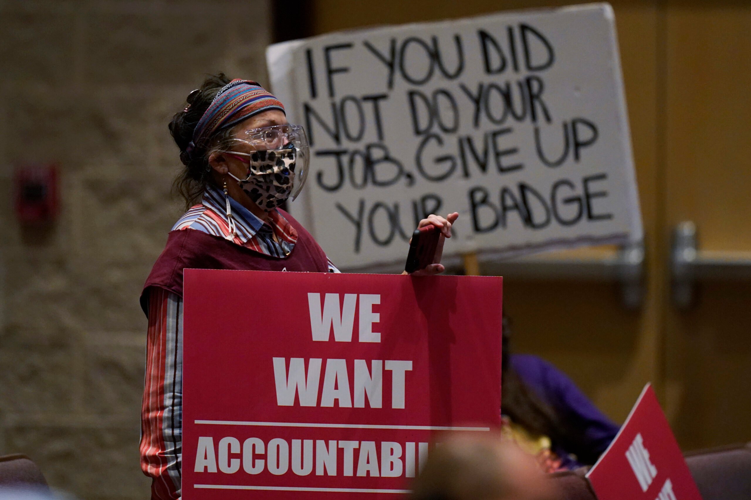 A protester holds a sign reading "If you did not do your job, give up your badge" at a meeting of the Board of Trustees of the Uvalde Consolidated Independent School District. A banner draped over the dais reads, "We want accountability."